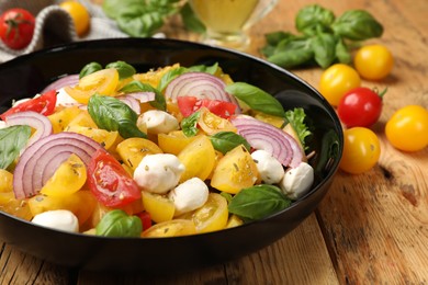 Photo of Tasty salad with yellow tomatoes, basil, onion and mozzarella cheese on wooden table, closeup