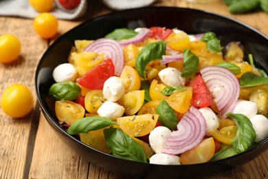 Photo of Tasty salad with yellow tomatoes, basil, onion and mozzarella cheese on wooden table, closeup