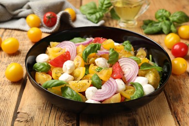 Photo of Tasty salad with yellow tomatoes, basil, onion and mozzarella cheese on wooden table, closeup