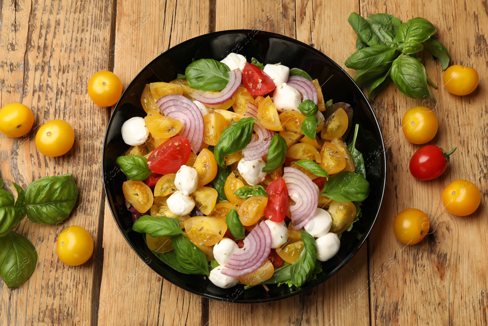Tasty salad with yellow tomatoes, basil, onion and mozzarella cheese on wooden table, flat lay Photo of Tasty salad with yellow tomatoes, basil, onion and mozzarella cheese on wooden table, flat lay