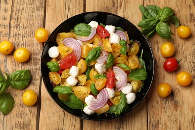 Photo of Tasty salad with yellow tomatoes, basil, onion and mozzarella cheese on wooden table, flat lay