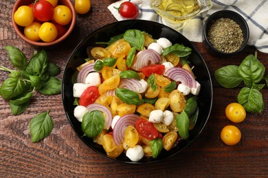 Photo of Tasty salad with yellow tomatoes, basil, onion and mozzarella cheese on wooden table, flat lay