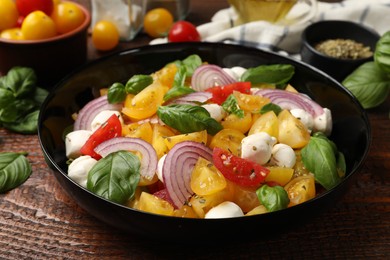 Photo of Tasty salad with yellow tomatoes, basil, onion and mozzarella cheese on wooden table, closeup