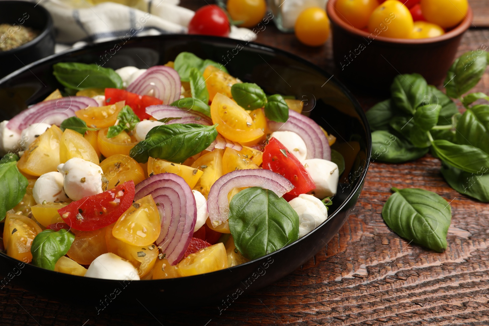 Tasty salad with yellow tomatoes, basil, onion and mozzarella cheese on wooden table, closeup Photo of Tasty salad with yellow tomatoes, basil, onion and mozzarella cheese on wooden table, closeup