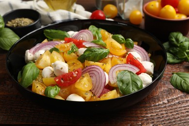 Photo of Tasty salad with yellow tomatoes, basil, onion and mozzarella cheese on wooden table, closeup