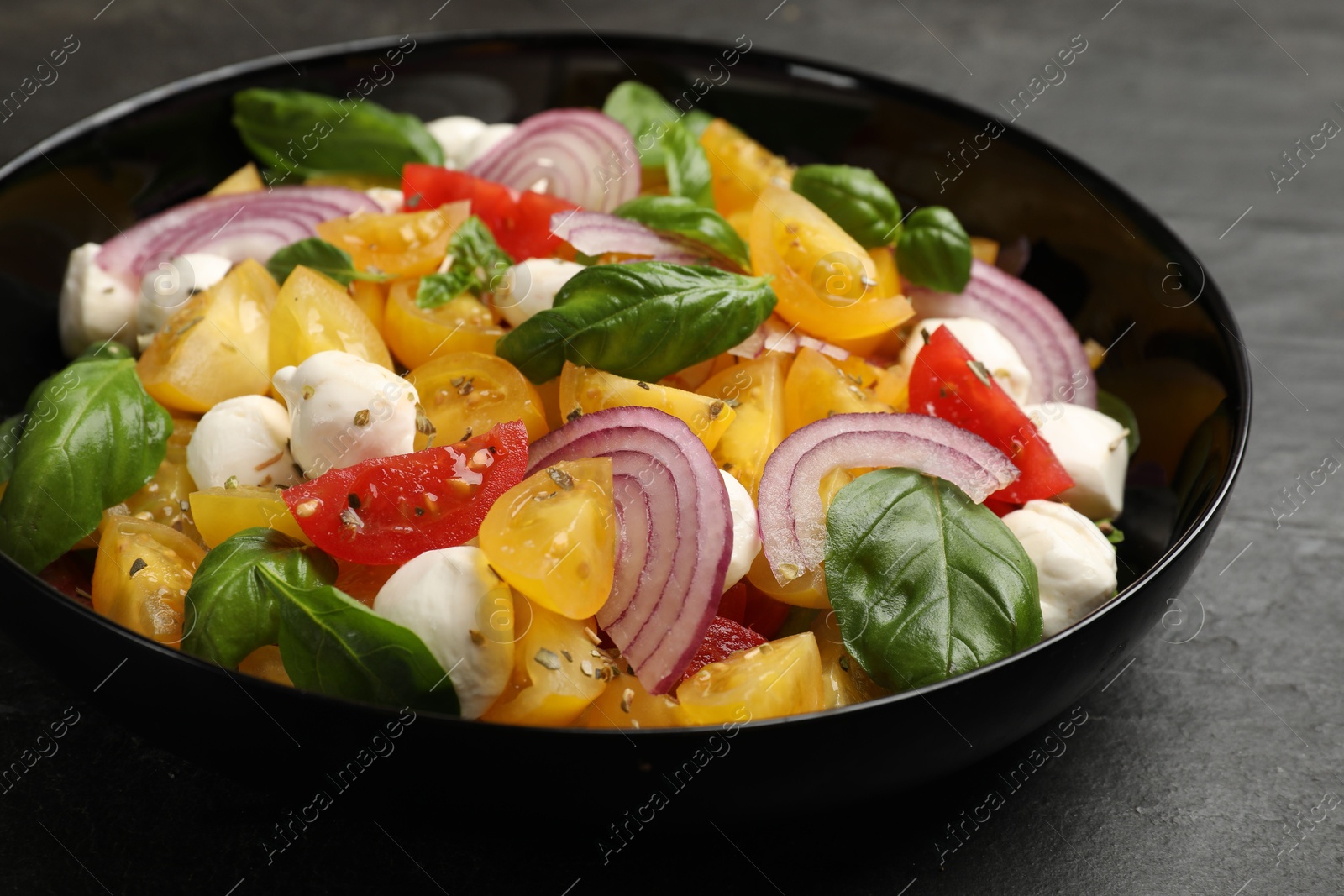 Tasty salad with yellow tomatoes, basil, onion and mozzarella cheese on black table, closeup Photo of Tasty salad with yellow tomatoes, basil, onion and mozzarella cheese on black table, closeup
