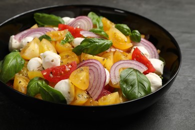 Photo of Tasty salad with yellow tomatoes, basil, onion and mozzarella cheese on black table, closeup
