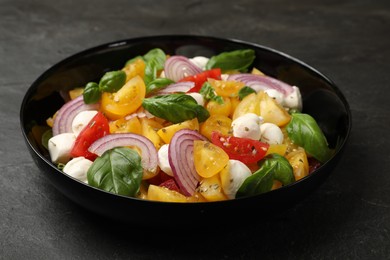 Photo of Tasty salad with yellow tomatoes, basil, onion and mozzarella cheese on black table, closeup