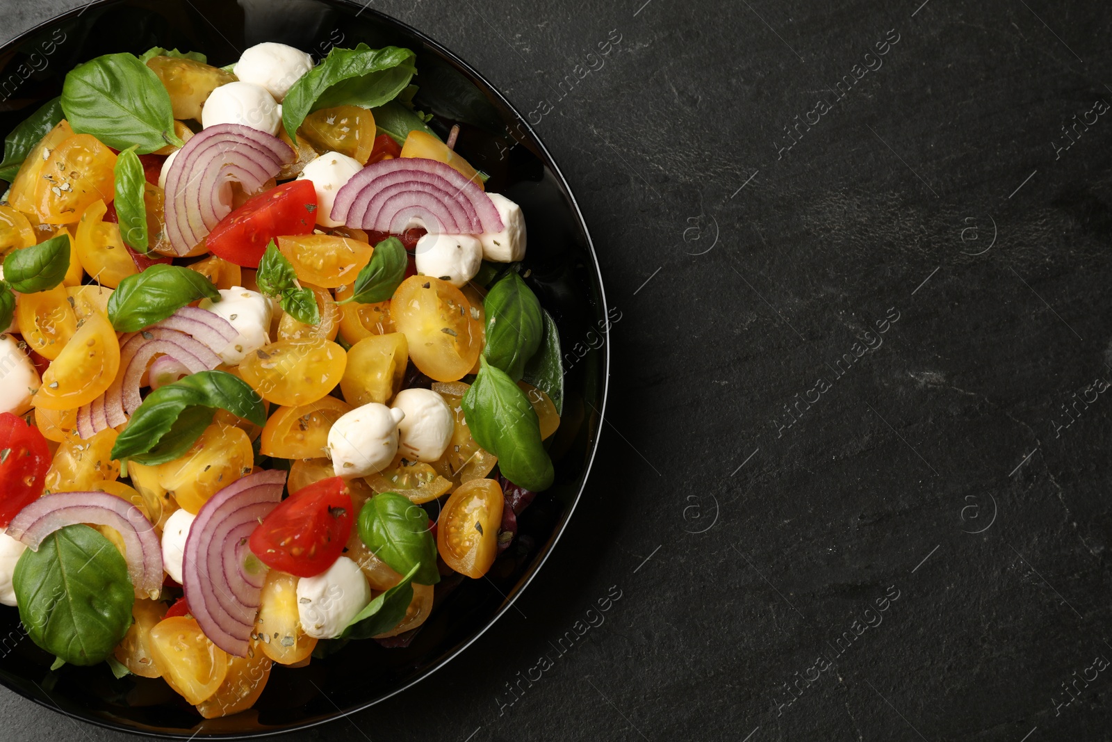 Tasty salad with yellow tomatoes, basil, onion and mozzarella cheese on black table, top view. Space for text Photo of Tasty salad with yellow tomatoes, basil, onion and mozzarella cheese on black table, top view. Space for text