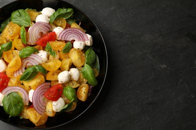 Photo of Tasty salad with yellow tomatoes, basil, onion and mozzarella cheese on black table, top view. Space for text