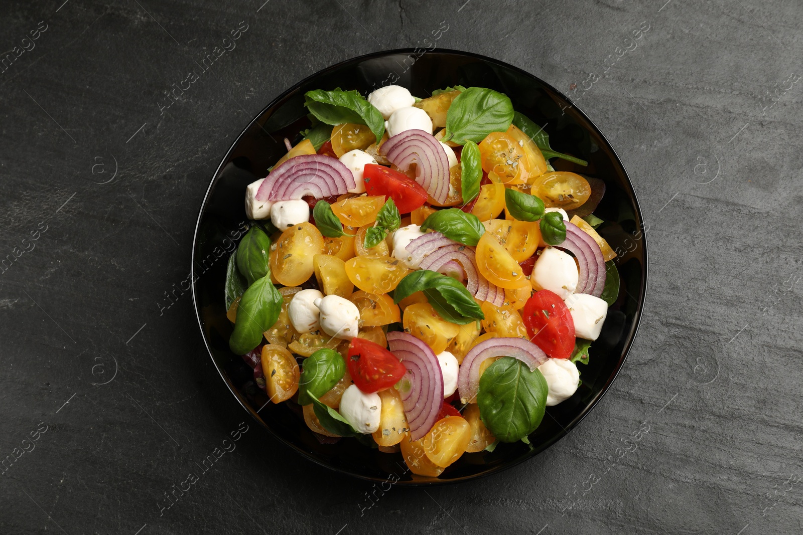 Tasty salad with yellow tomatoes, basil, onion and mozzarella cheese on black table, top view Photo of Tasty salad with yellow tomatoes, basil, onion and mozzarella cheese on black table, top view