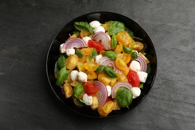 Photo of Tasty salad with yellow tomatoes, basil, onion and mozzarella cheese on black table, top view