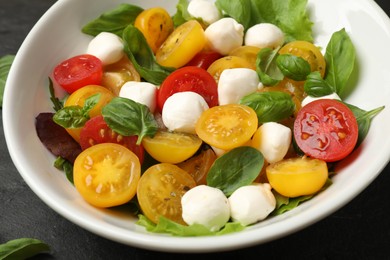 Photo of Tasty salad with yellow tomatoes, basil and mozzarella cheese on black table, closeup