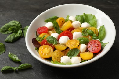 Photo of Tasty salad with yellow tomatoes, basil and mozzarella cheese on black table, closeup