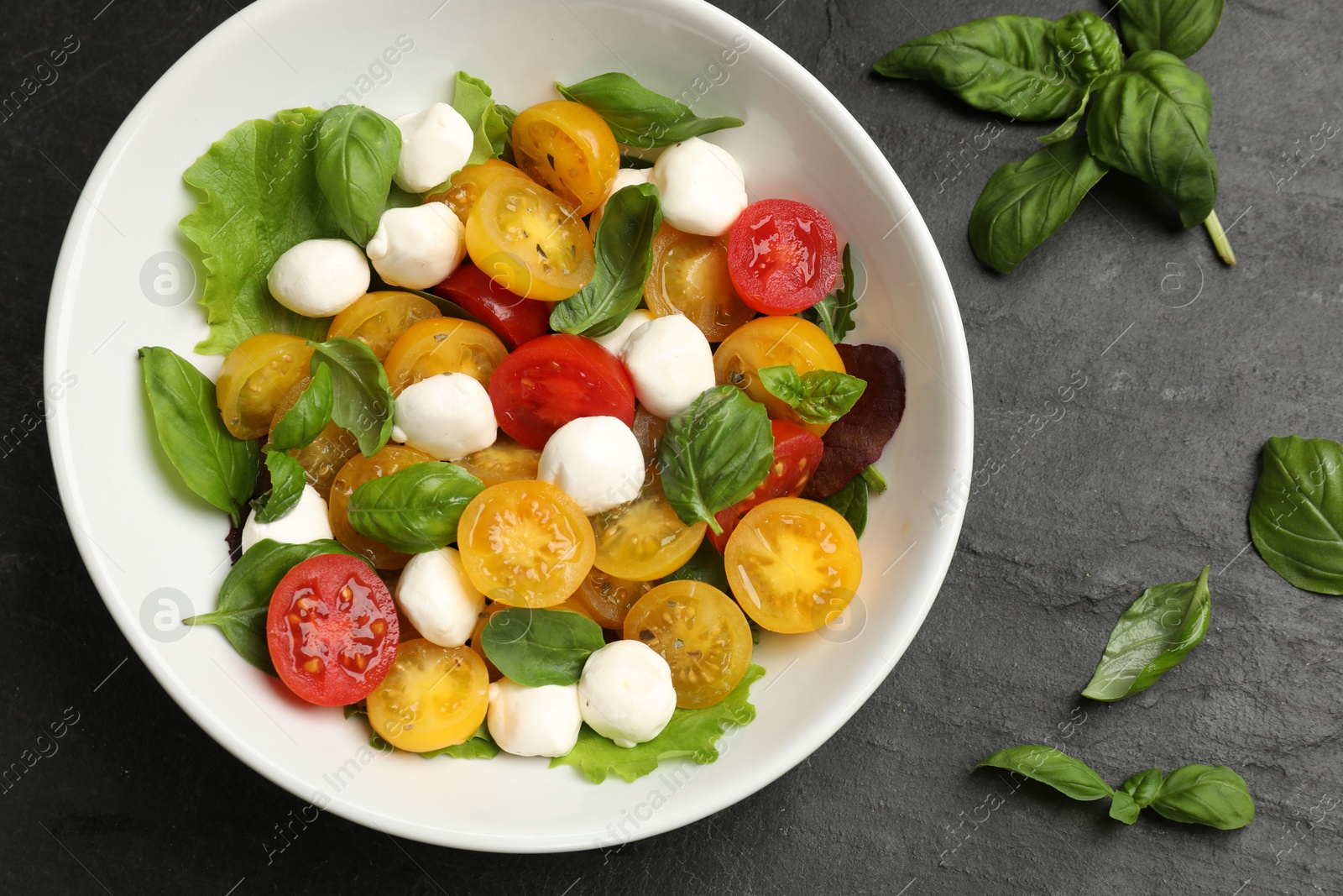 Tasty salad with yellow tomatoes, basil and mozzarella cheese on black table, flat lay Photo of Tasty salad with yellow tomatoes, basil and mozzarella cheese on black table, flat lay