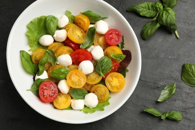 Photo of Tasty salad with yellow tomatoes, basil and mozzarella cheese on black table, flat lay