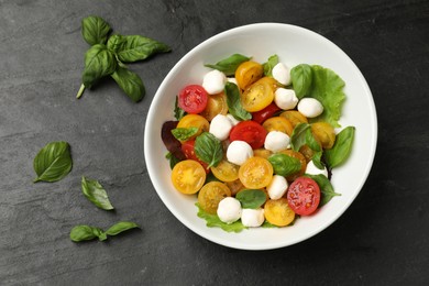 Photo of Tasty salad with yellow tomatoes, basil and mozzarella cheese on black table, flat lay