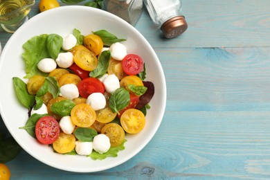 Photo of Tasty salad with yellow tomatoes, basil and mozzarella cheese on light blue wooden table, flat lay. Space for text
