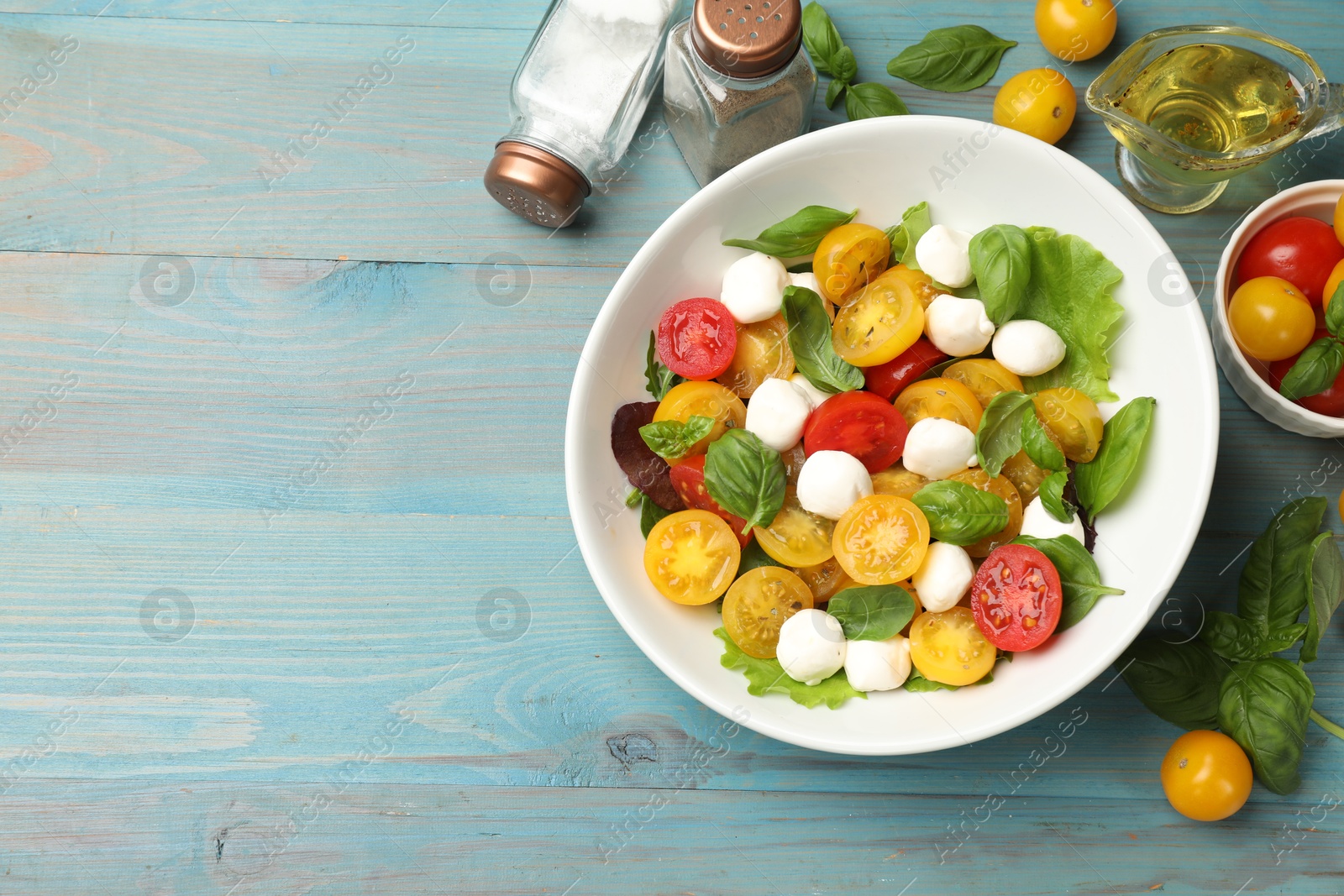 Tasty salad with yellow tomatoes, basil and mozzarella cheese on light blue wooden table, flat lay. Space for text Photo of Tasty salad with yellow tomatoes, basil and mozzarella cheese on light blue wooden table, flat lay. Space for text
