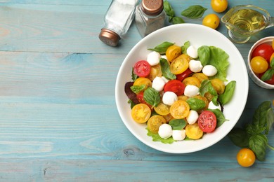 Photo of Tasty salad with yellow tomatoes, basil and mozzarella cheese on light blue wooden table, flat lay. Space for text