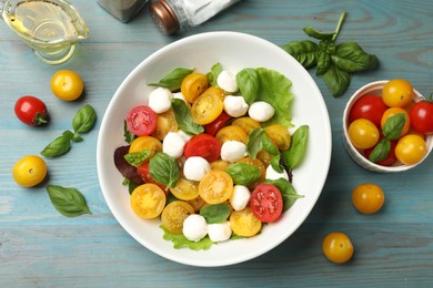Photo of Tasty salad with yellow tomatoes, basil and mozzarella cheese on light blue wooden table, flat lay
