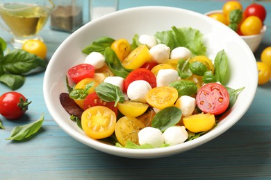 Photo of Tasty salad with yellow tomatoes, basil and mozzarella cheese on light blue wooden table, closeup
