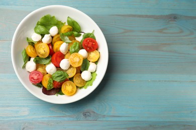 Photo of Tasty salad with yellow tomatoes, basil and mozzarella cheese on light blue wooden table, top view. Space for text