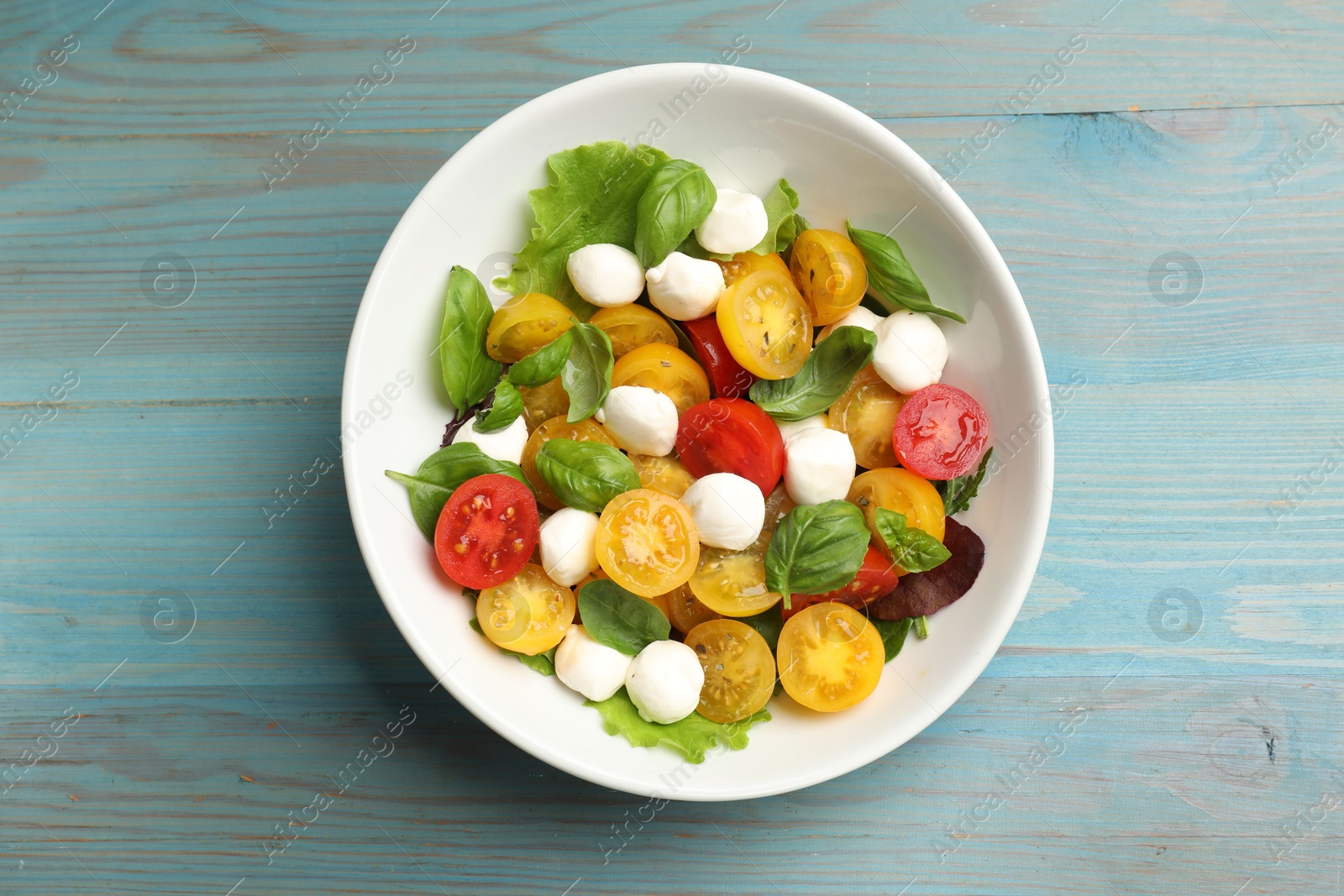 Tasty salad with yellow tomatoes, basil and mozzarella cheese on light blue wooden table, top view Photo of Tasty salad with yellow tomatoes, basil and mozzarella cheese on light blue wooden table, top view