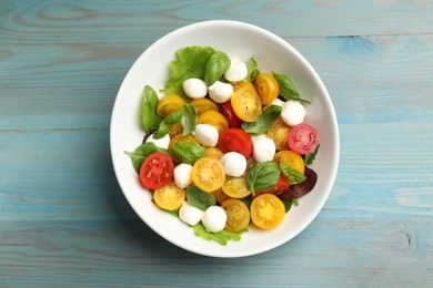 Photo of Tasty salad with yellow tomatoes, basil and mozzarella cheese on light blue wooden table, top view