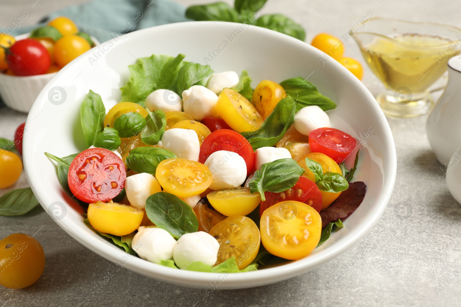 Tasty salad with yellow tomatoes, basil and mozzarella cheese on light grey table, closeup Photo of Tasty salad with yellow tomatoes, basil and mozzarella cheese on light grey table, closeup