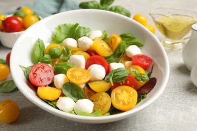 Photo of Tasty salad with yellow tomatoes, basil and mozzarella cheese on light grey table, closeup