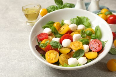 Photo of Tasty salad with yellow tomatoes, basil and mozzarella cheese on light grey table, closeup