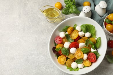Photo of Tasty salad with yellow tomatoes, basil and mozzarella cheese on light grey table, flat lay. Space for text