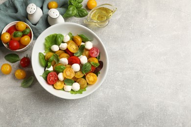 Photo of Tasty salad with yellow tomatoes, basil and mozzarella cheese on light grey table, flat lay. Space for text