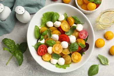 Photo of Tasty salad with yellow tomatoes, basil and mozzarella cheese on light grey table, flat lay