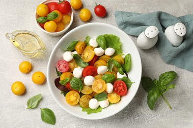 Photo of Tasty salad with yellow tomatoes, basil and mozzarella cheese on light grey table, flat lay