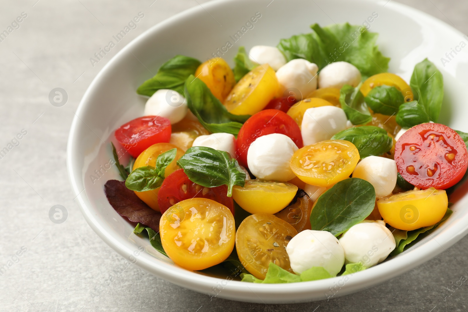Tasty salad with yellow tomatoes, basil and mozzarella cheese on light grey table, closeup Photo of Tasty salad with yellow tomatoes, basil and mozzarella cheese on light grey table, closeup