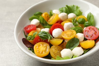 Photo of Tasty salad with yellow tomatoes, basil and mozzarella cheese on light grey table, closeup