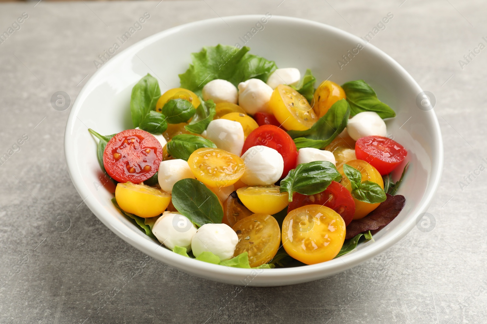 Tasty salad with yellow tomatoes, basil and mozzarella cheese on light grey table, closeup Photo of Tasty salad with yellow tomatoes, basil and mozzarella cheese on light grey table, closeup