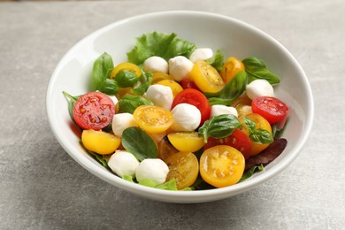 Photo of Tasty salad with yellow tomatoes, basil and mozzarella cheese on light grey table, closeup
