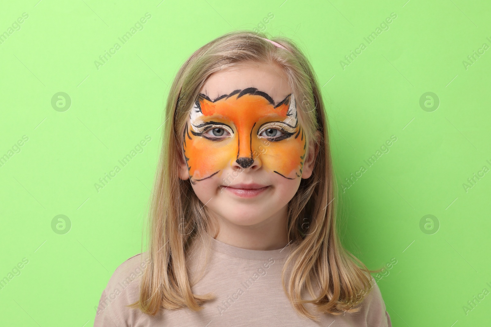 Cute girl with fox face painting on light green background Photo of Cute girl with fox face painting on light green background