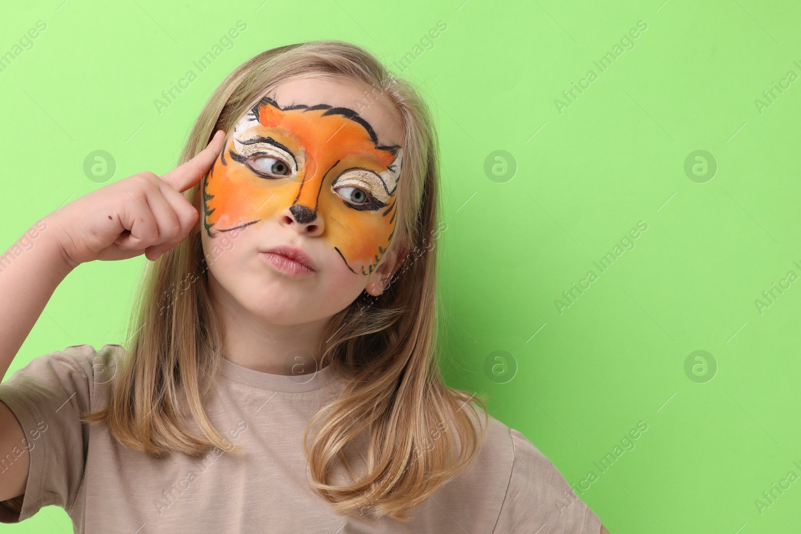 Cute girl with fox face painting on light green background, space for text Photo of Cute girl with fox face painting on light green background, space for text