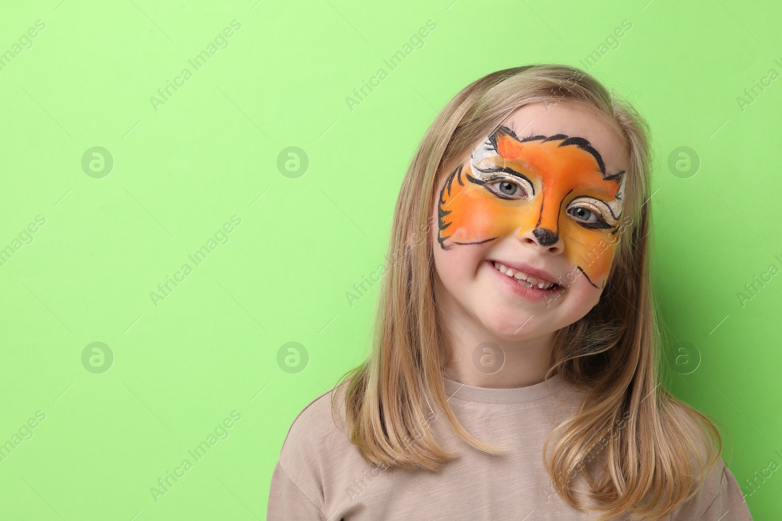 Cute girl with fox face painting on light green background, space for text Photo of Cute girl with fox face painting on light green background, space for text