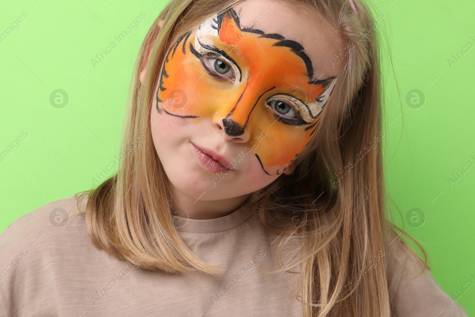 Cute girl with fox face painting on light green background Photo of Cute girl with fox face painting on light green background