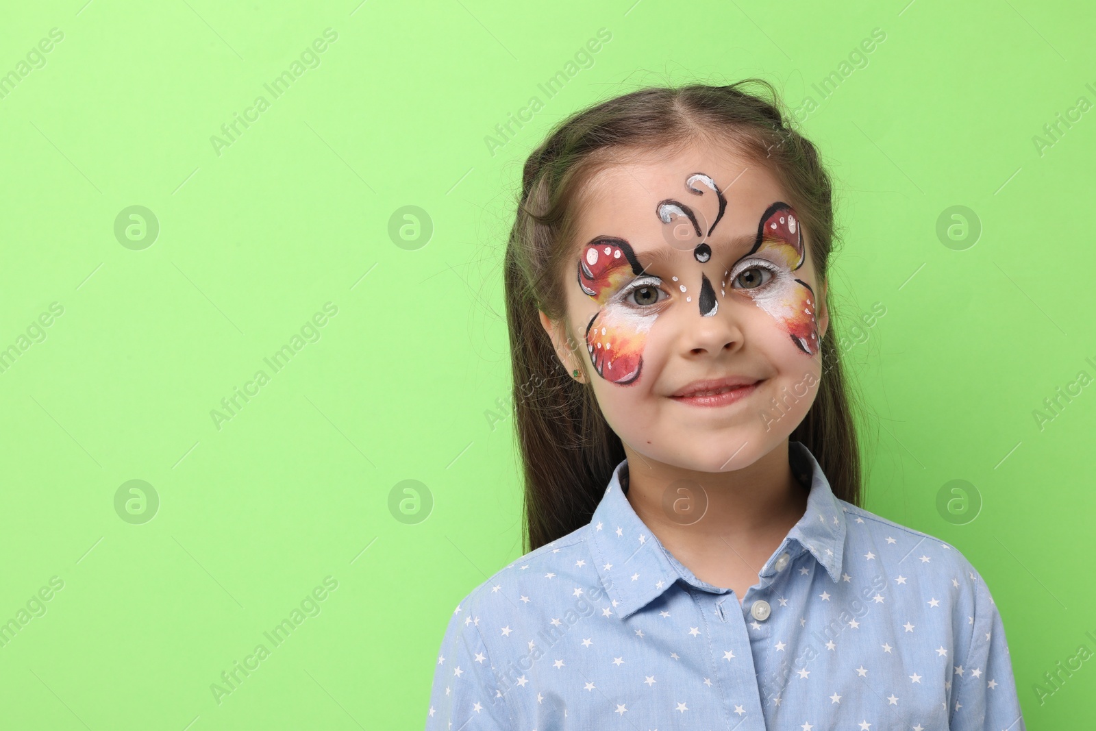 Cute girl with butterfly face painting on light green background, space for text Photo of Cute girl with butterfly face painting on light green background, space for text