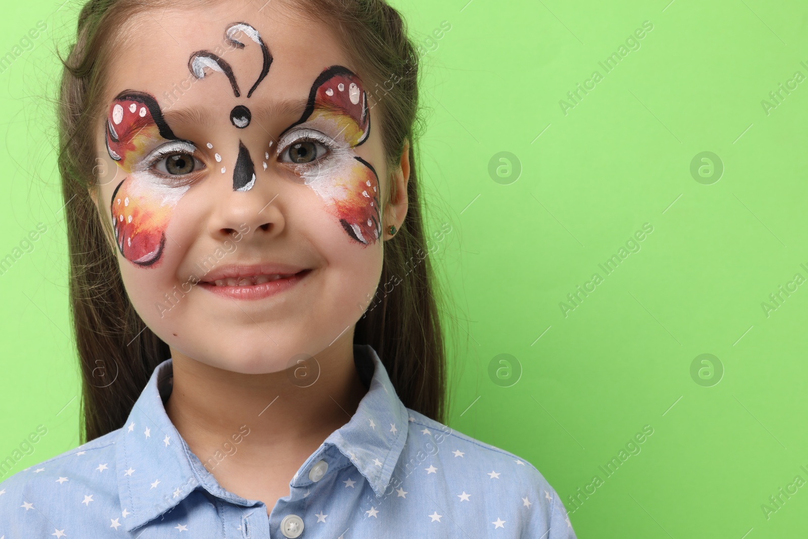 Cute girl with butterfly face painting on light green background, space for text Photo of Cute girl with butterfly face painting on light green background, space for text