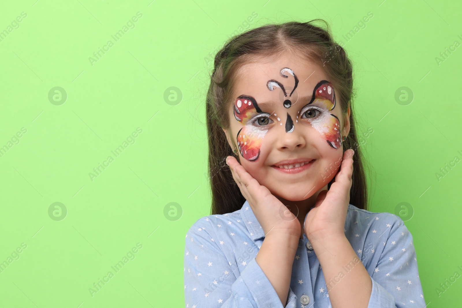 Cute girl with butterfly face painting on light green background, space for text Photo of Cute girl with butterfly face painting on light green background, space for text