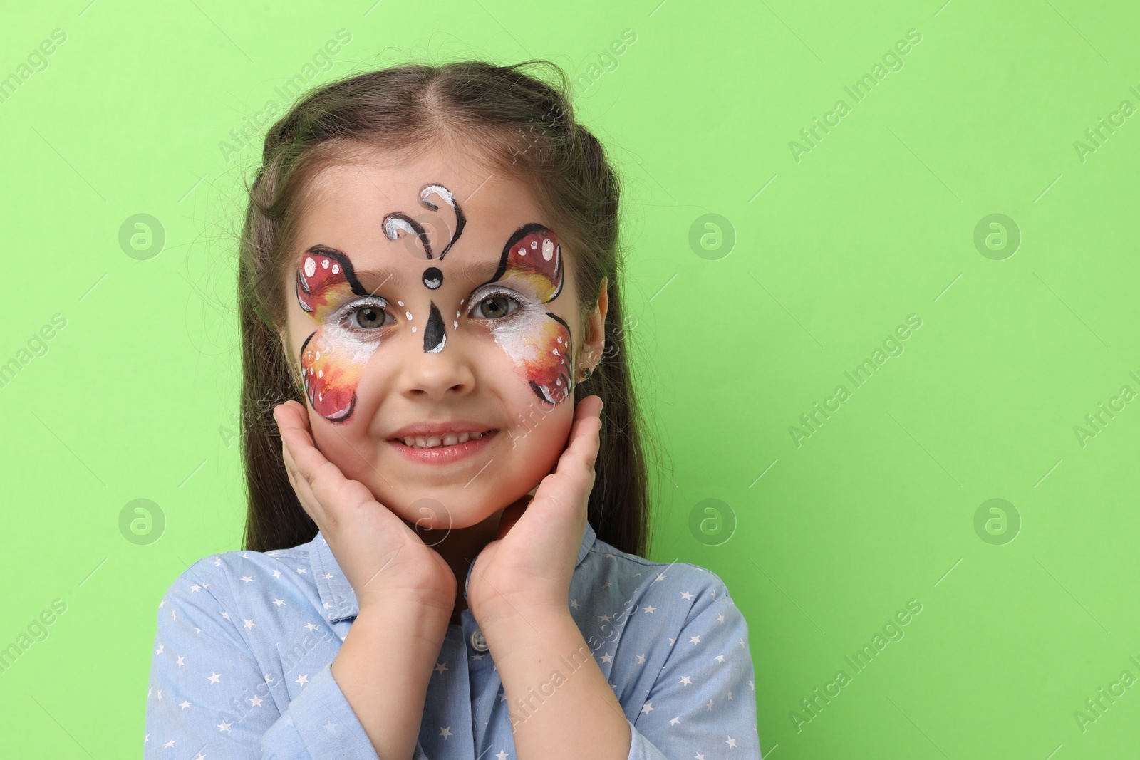 Cute girl with butterfly face painting on light green background, space for text Photo of Cute girl with butterfly face painting on light green background, space for text
