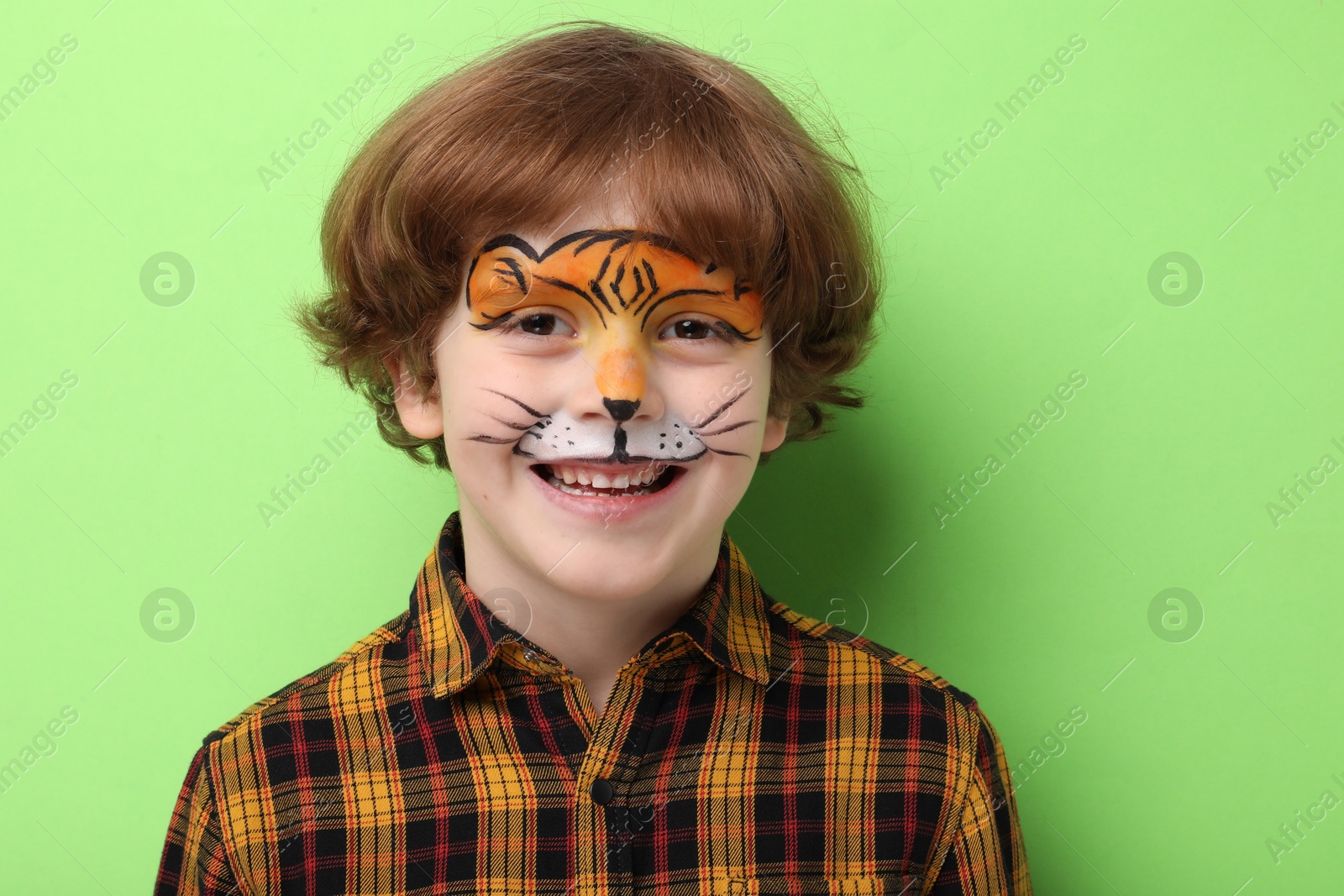 Cute boy with tiger face painting on light green background Photo of Cute boy with tiger face painting on light green background