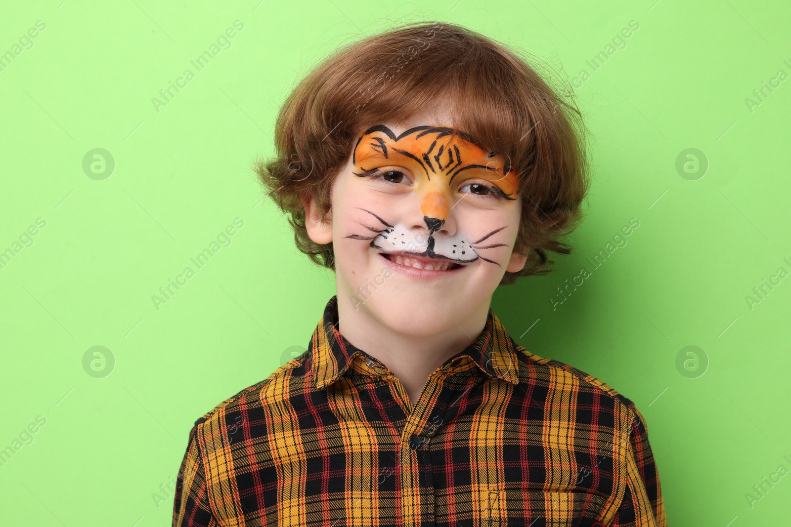 Cute boy with tiger face painting on light green background Photo of Cute boy with tiger face painting on light green background